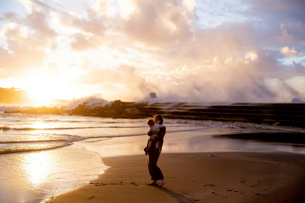 A heartwarming scene of a mother carrying her child by the sea at sunset.